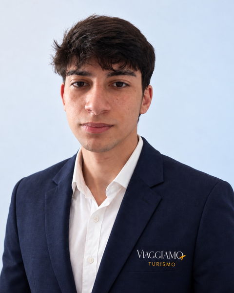 Caio, consultor de viagens da Viaggiamo, de blazer azul-marinho com o logotipo da agência.